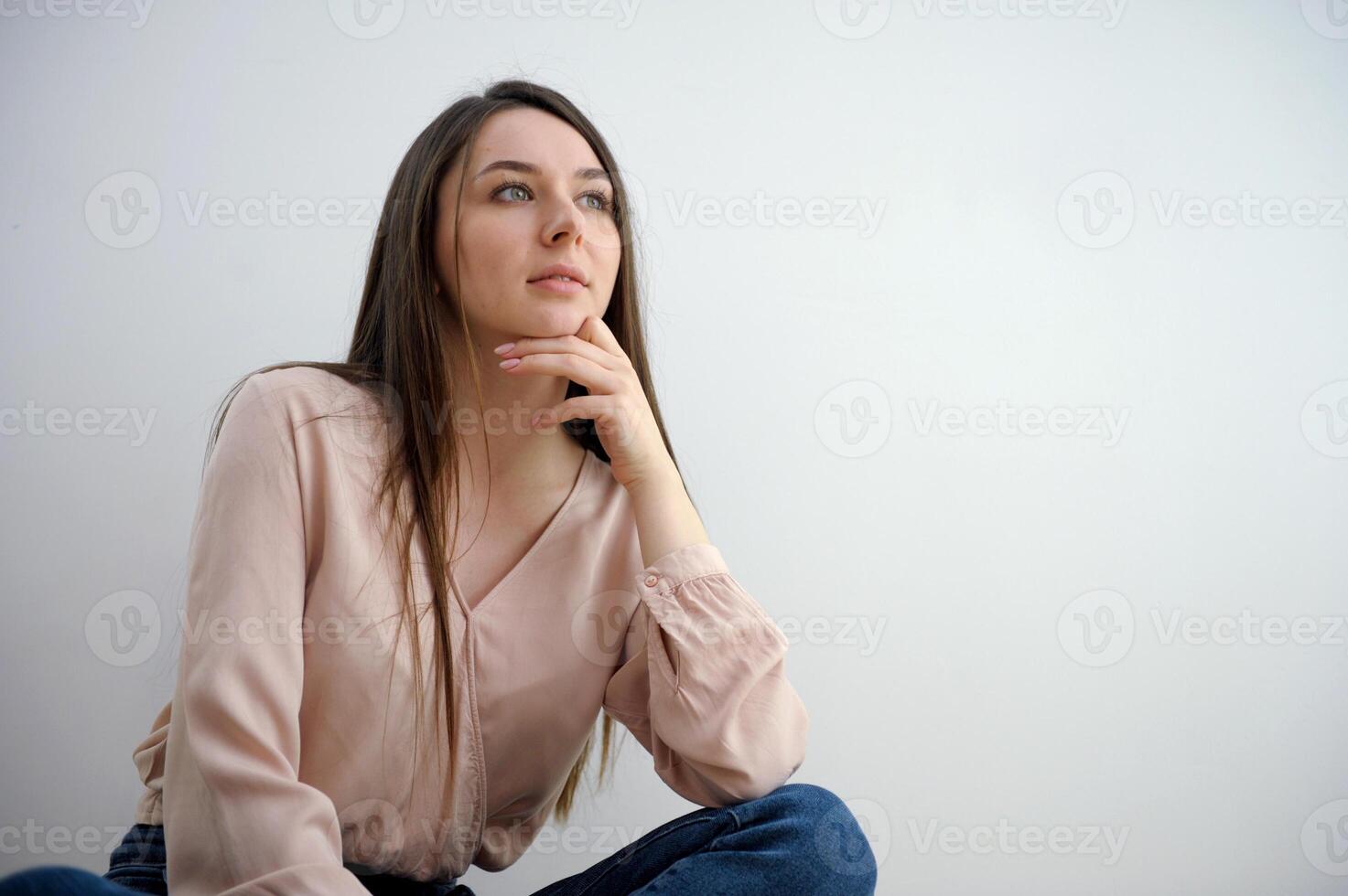 businesswoman thinking and sitting at her desk isolated on white background Pensive brunette woman in sweater holding her chin and looking up over grey background photo