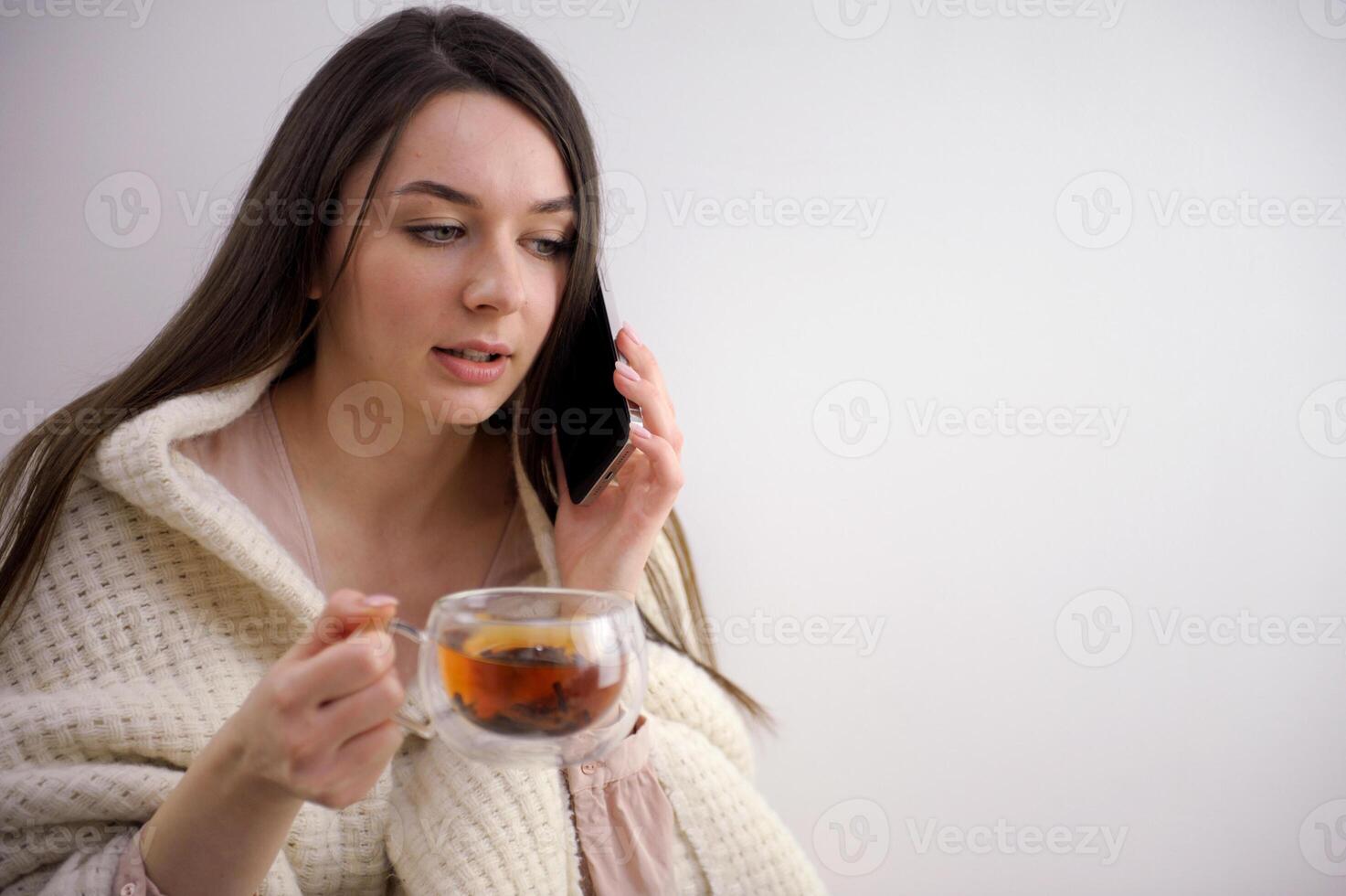 sick elegant 20 years old housewife in roll neck sweater and cardigan drinking cup of hot tea with ginger, lemon and honey against winter light blue background. photo