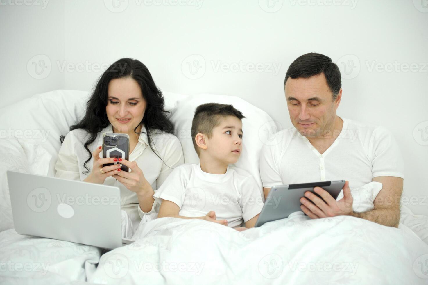 people, family and technology concept happy mother, father and little boy with tablet pc computer in bed at home or hotel room photo