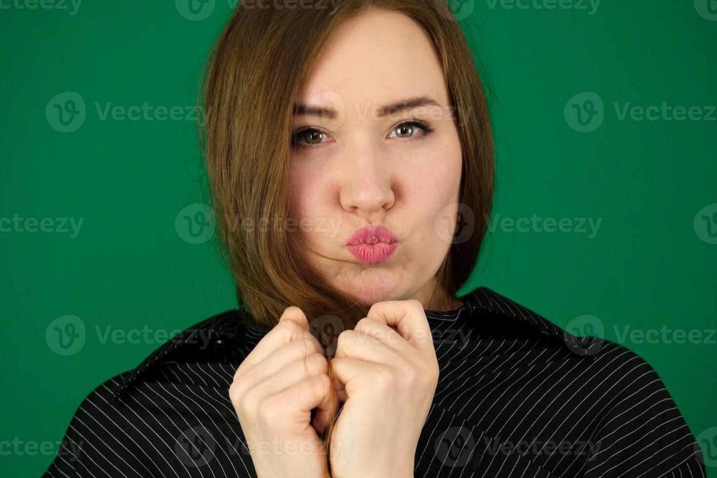beautiful girl blow kisses woman on a green background chromakey in a black striped mens shirt different emotions facial expression close-up advertising space for text clean. kind eyes photo