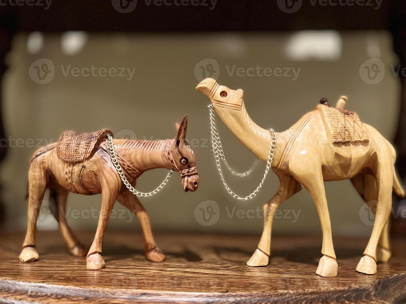 Two sculptures of a donkey and a camel, two wooden sculptures, stand opposite each other on a wooden shelf. They look at each other, each of them has a chain around their neck. photo
