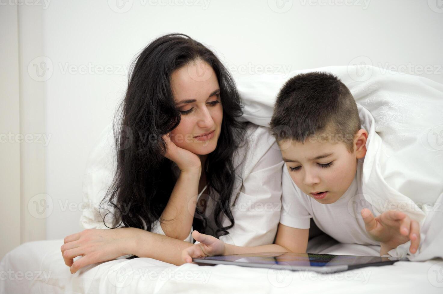 boy, And his mother is working on a laptop computer, The little boy put the tablet in his hand and turned to his busy mother intently, wanting his mother to pay attention to him. photo