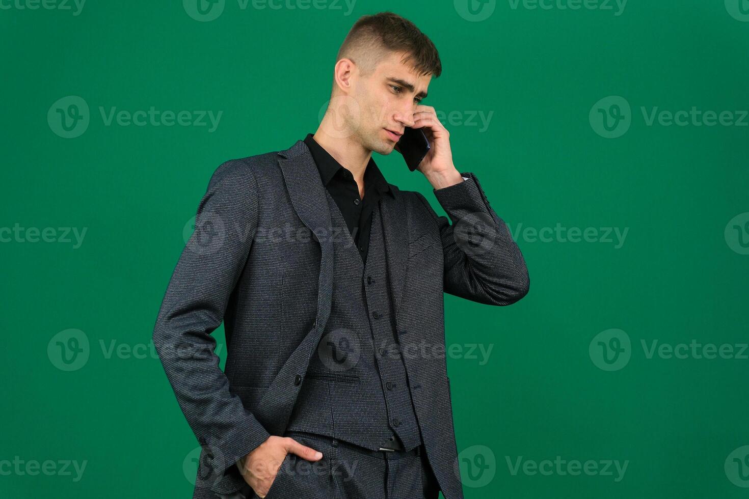 business man talking on a mobile phone in a black suit. emotions of a handsome man guy on a green background chromakey close-up dark hair young man. phone in hand talk dial SMS online call gadget boss photo