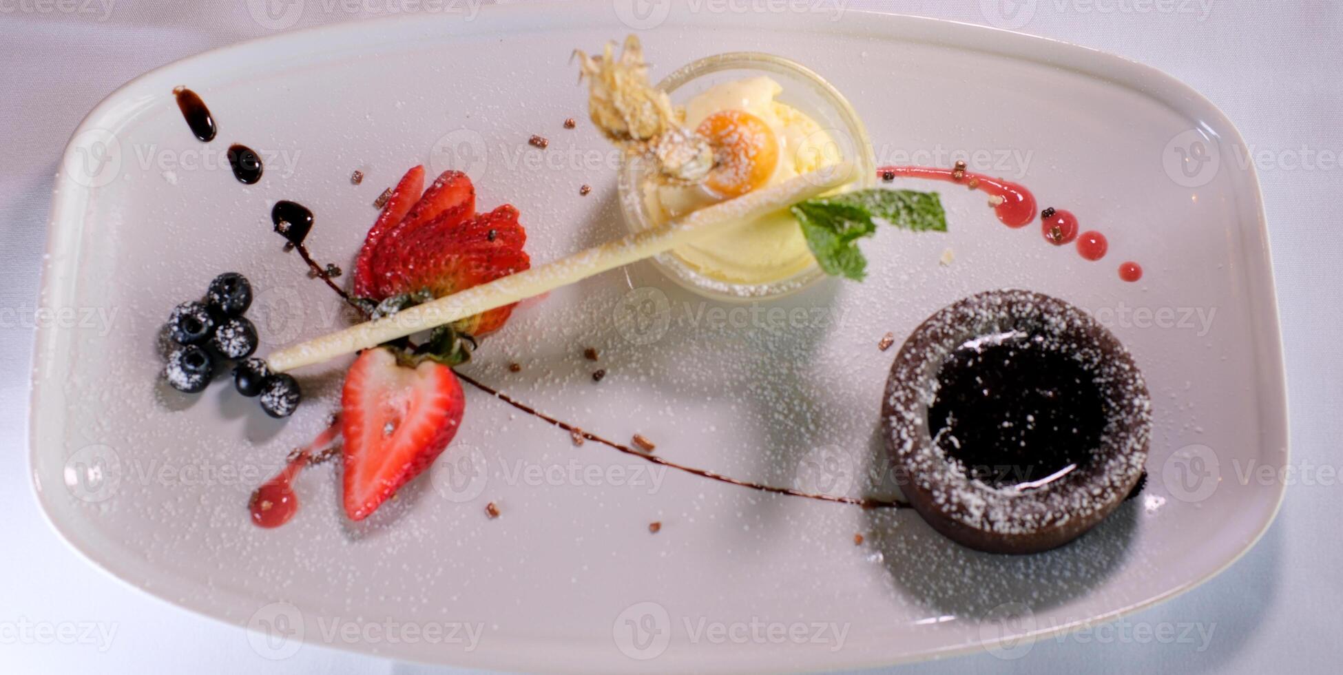 chocolate fondant on a white plate with dark chocolate ice cream strawberries drops of syrup beautiful serving in an expensive restaurant dessert food photo