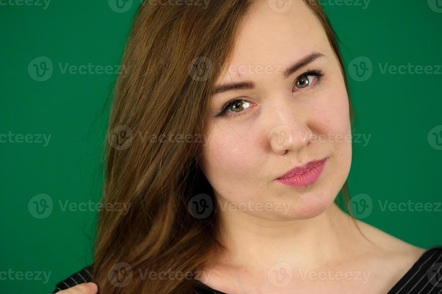 A studio close-up of a lovely young brunette. woman on green background chromakey in black striped mens shirt different emotions facial expression close-up advertising space for text clean. kind eyes photo