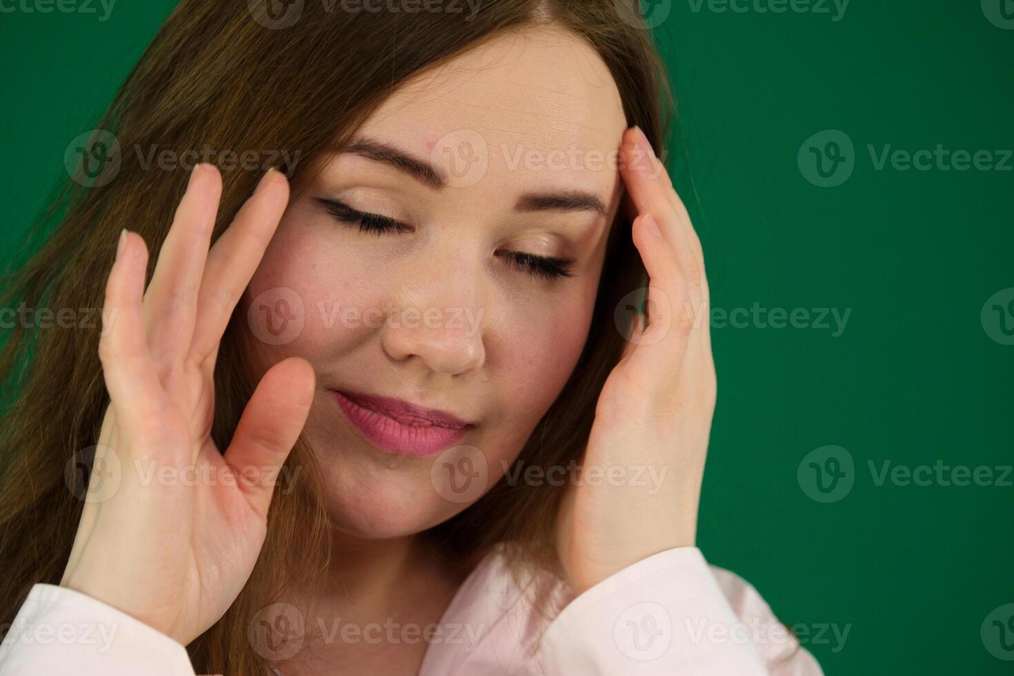 A young woman with a headache holding head, young girl woman with a pink beret on her head France fashion on a green background chromakey. different emotions pink jacket gloves long brown hair photo