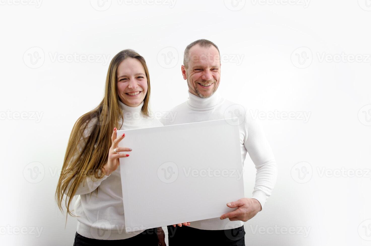 adult man and a young woman holding a picture in their hands a frame for advertising text smiling sincere laughter white clothes white background place empty frame paper cardboard poster banner photo