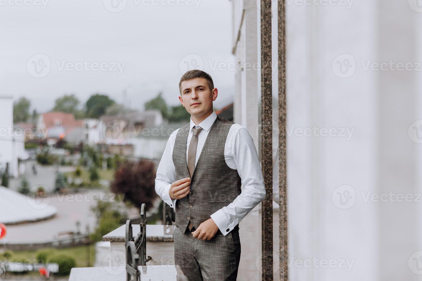 A man in a suit and vest stands on a balcony looking out over a city photo