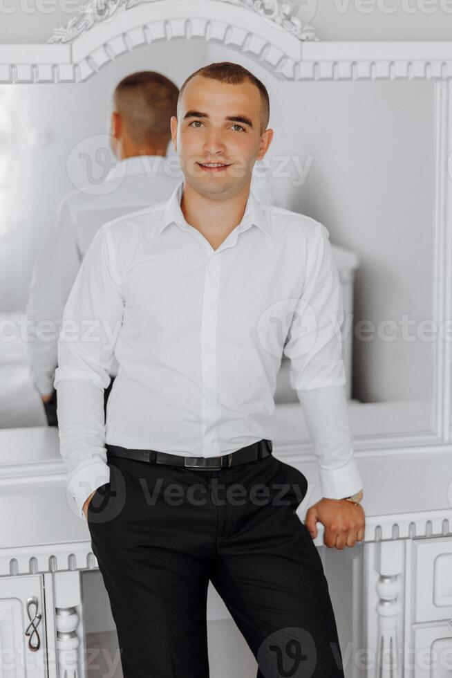 A man in a white shirt and black pants stands in front of a mirror photo