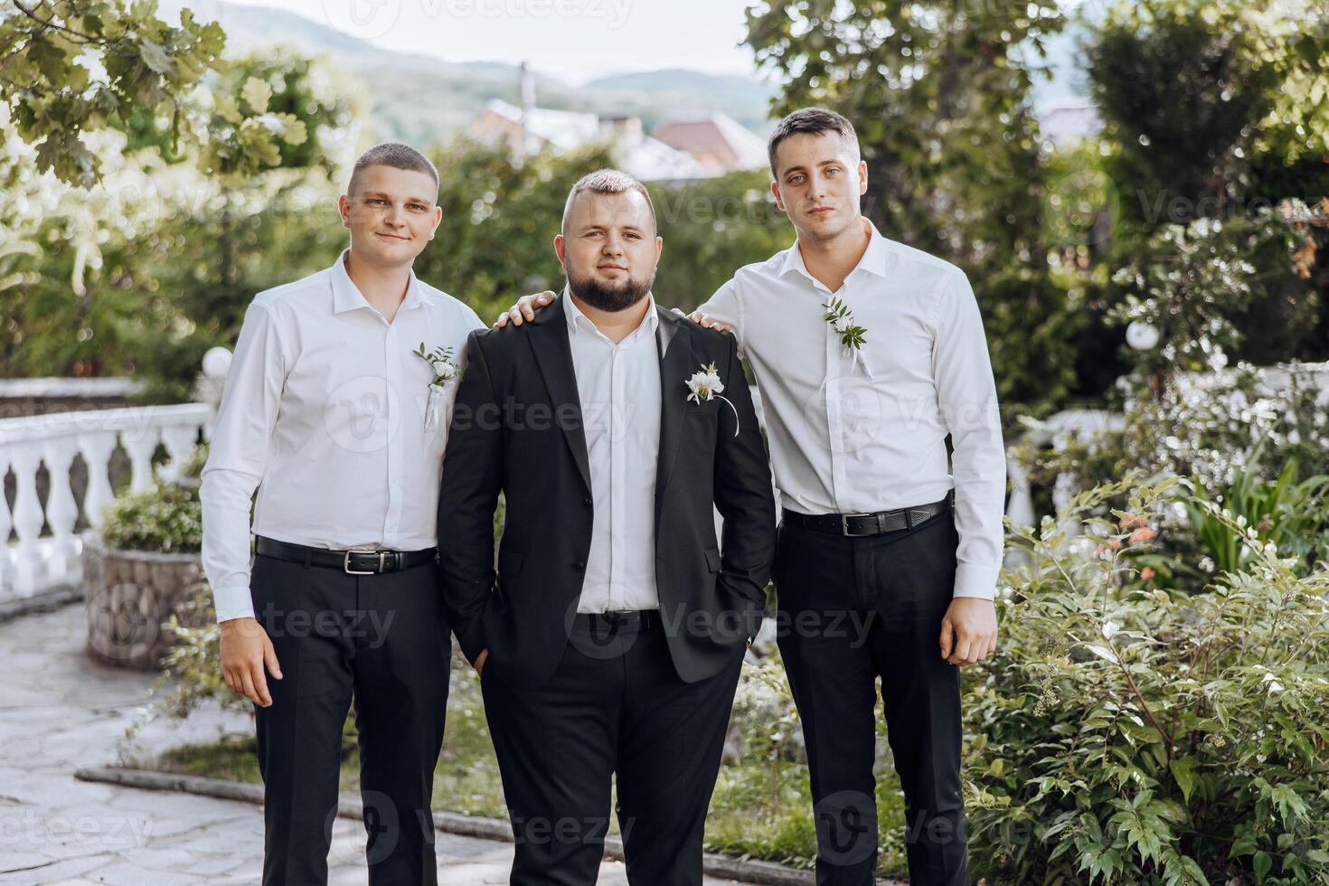 Three men in suits pose for a photo in front of a garden