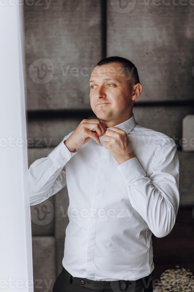 A man in a white shirt is getting dressed in front of a window photo