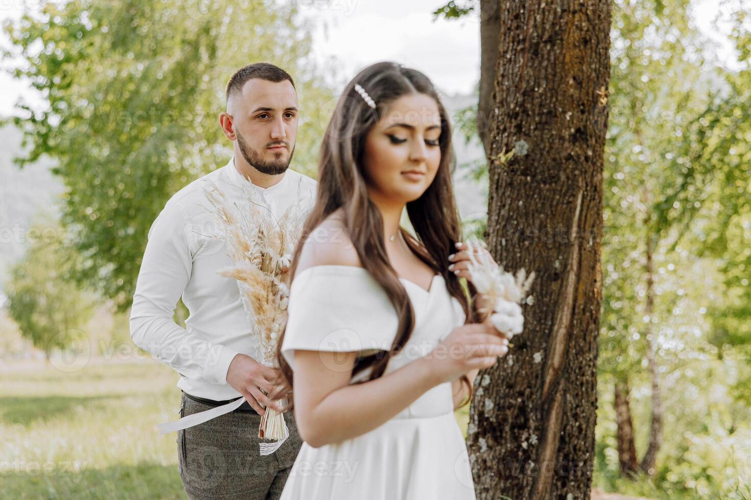 A man and a woman are standing in a field with a tree behind them photo