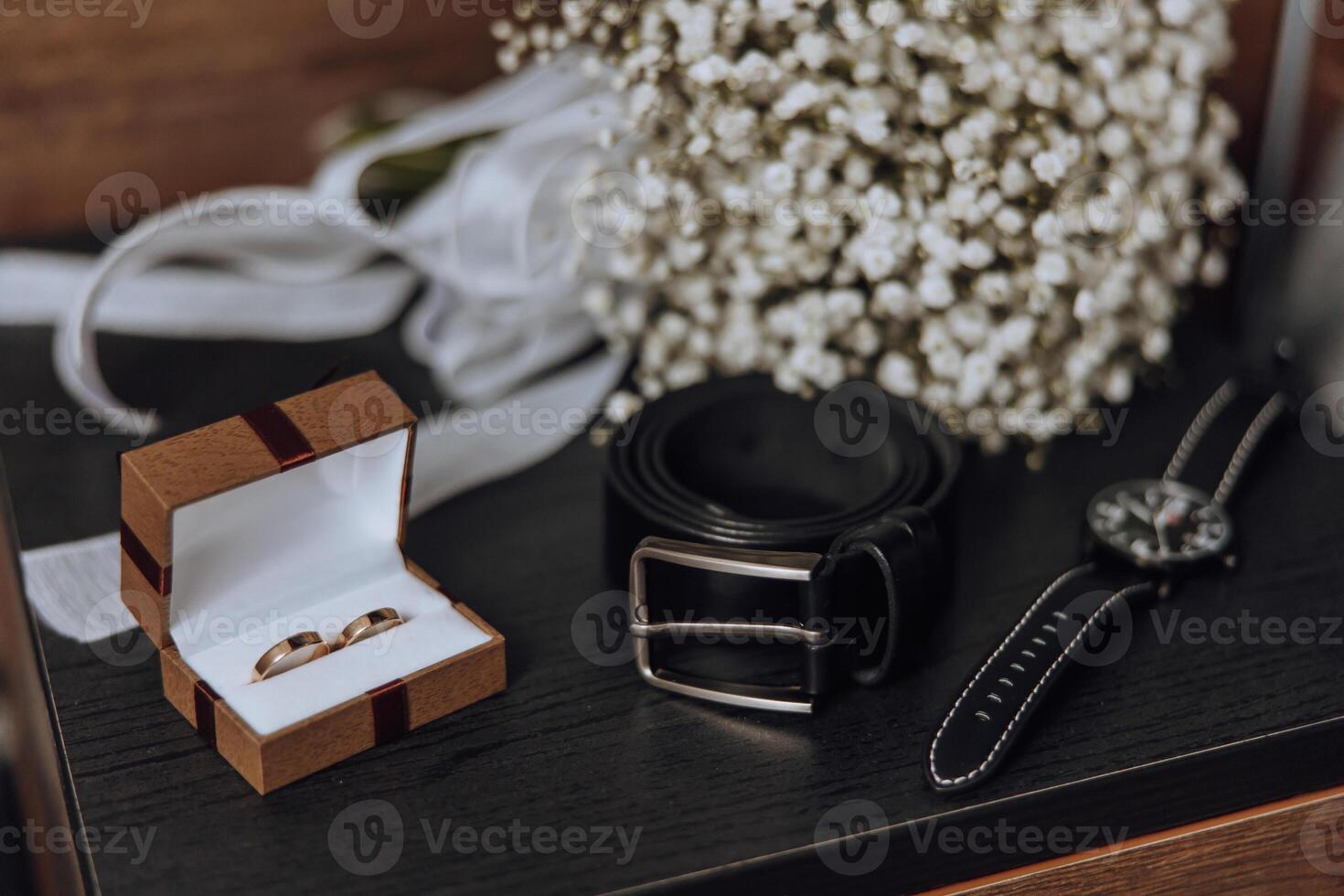 A wedding ring and a watch are displayed on a table photo
