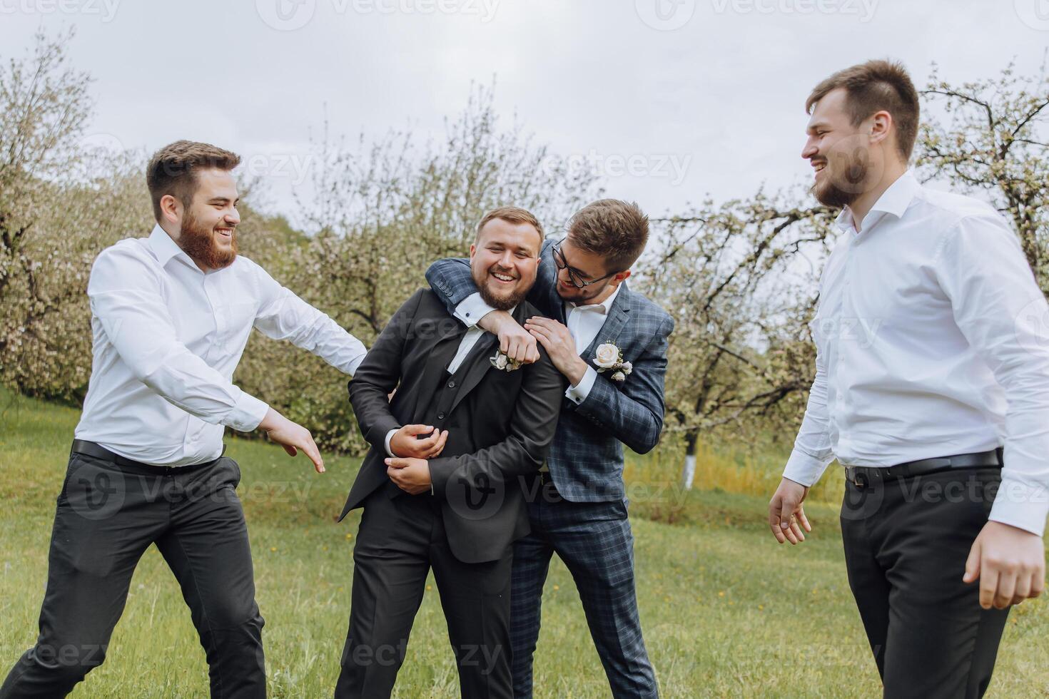four boys dressed in suits and white shirts, having fun in nature. The groom and his friends are celebrating a special event photo