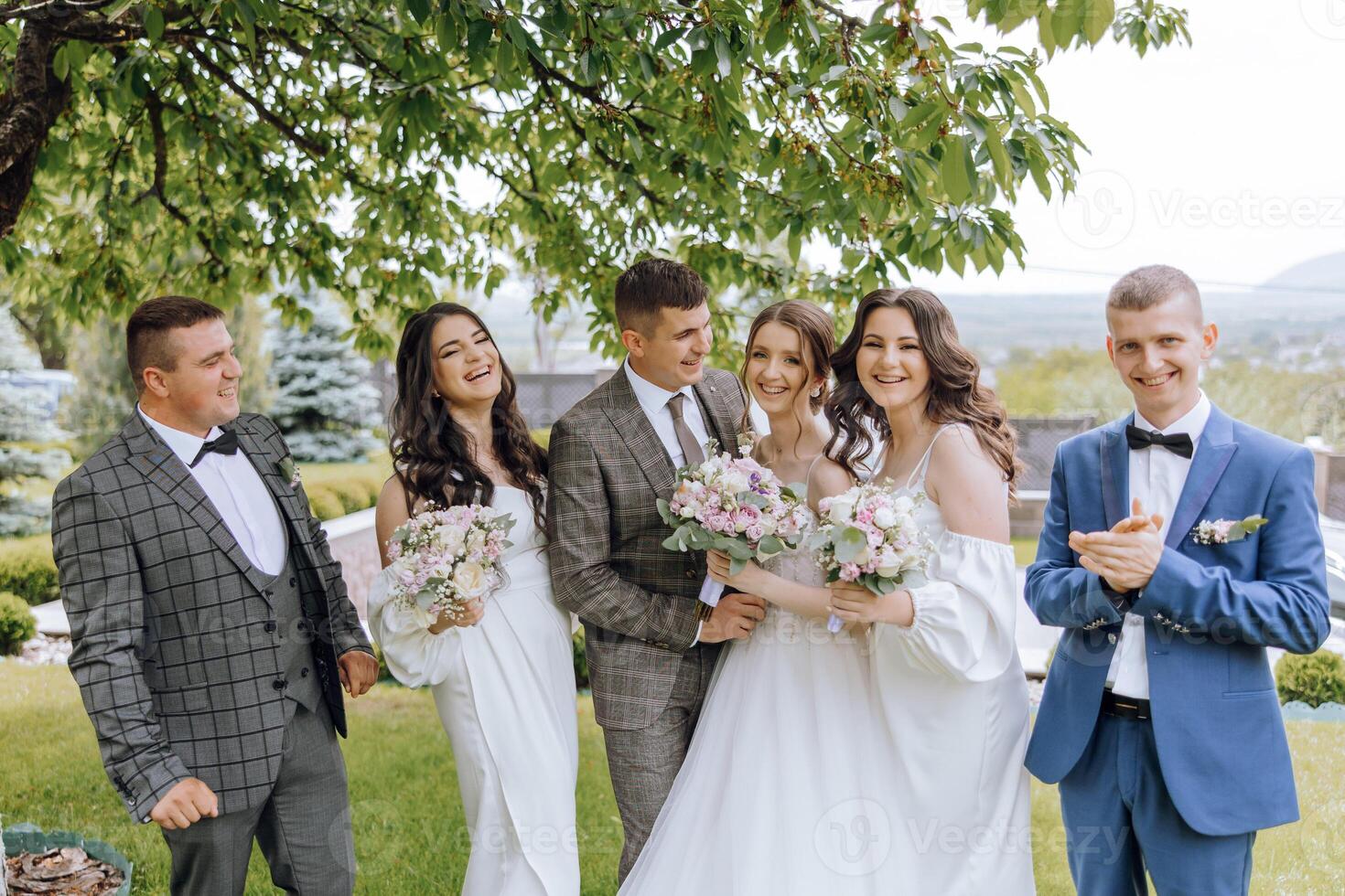 A group of people, including a bride and groom, are posing for a photo in a park