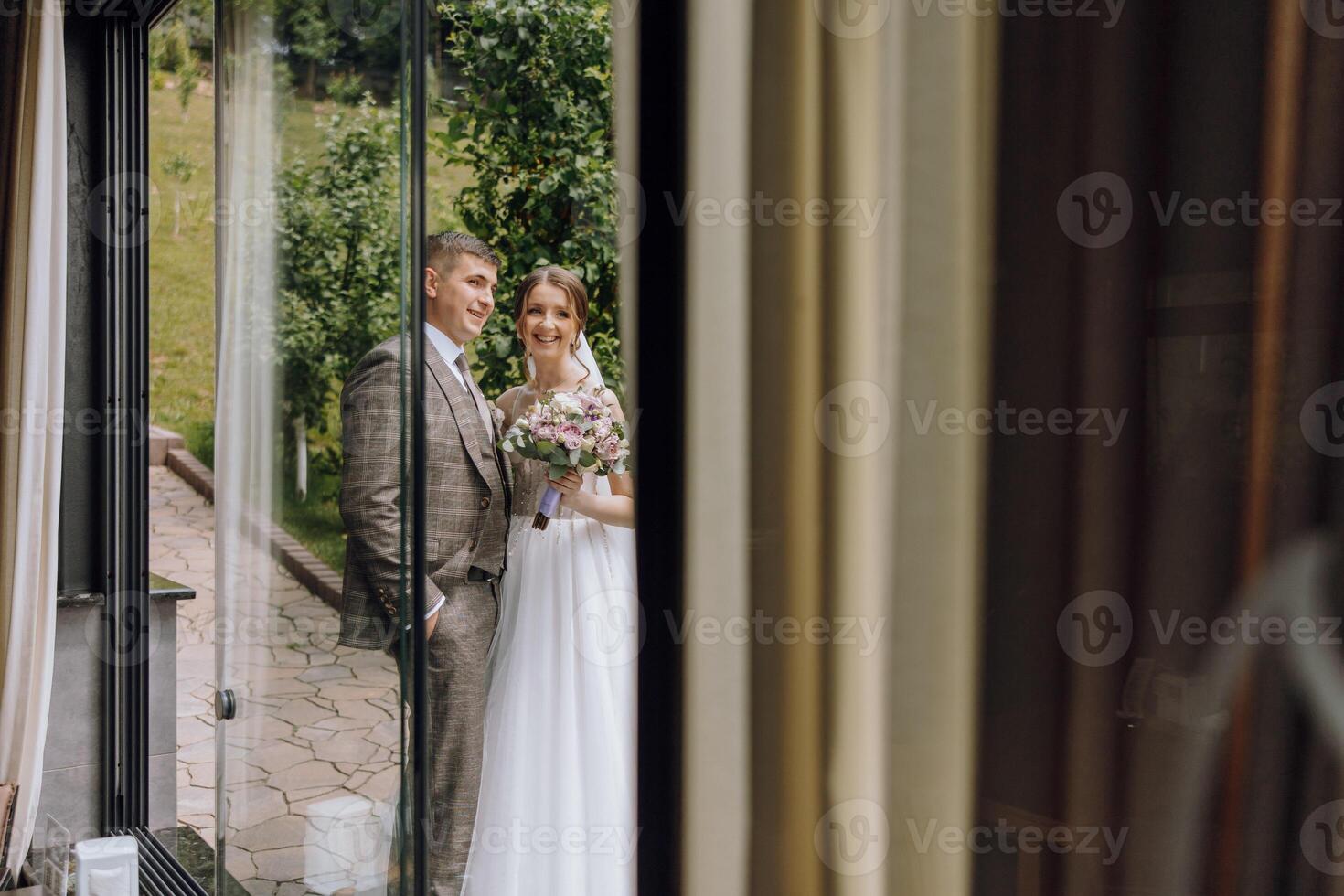 A bride and groom stand in front of a window, looking out at the world photo