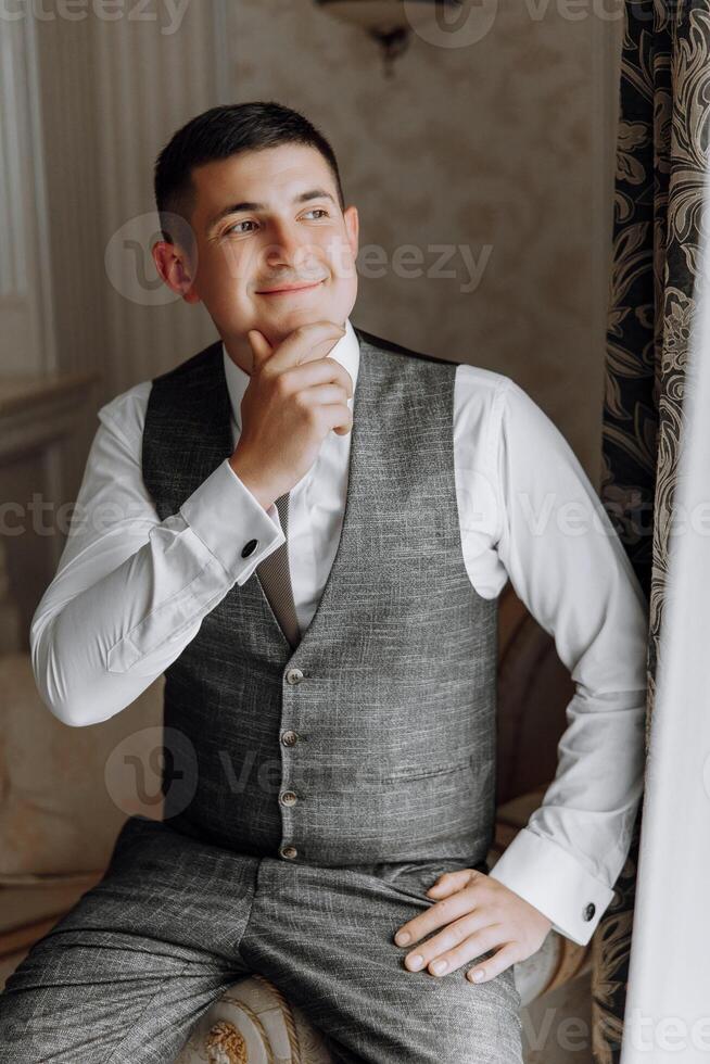 A man in a suit and vest is sitting on a couch and looking out the window photo