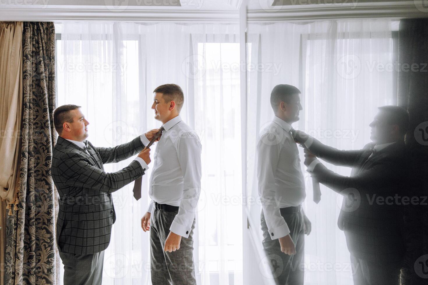 Two men are getting dressed up, one of them is wearing a tie photo