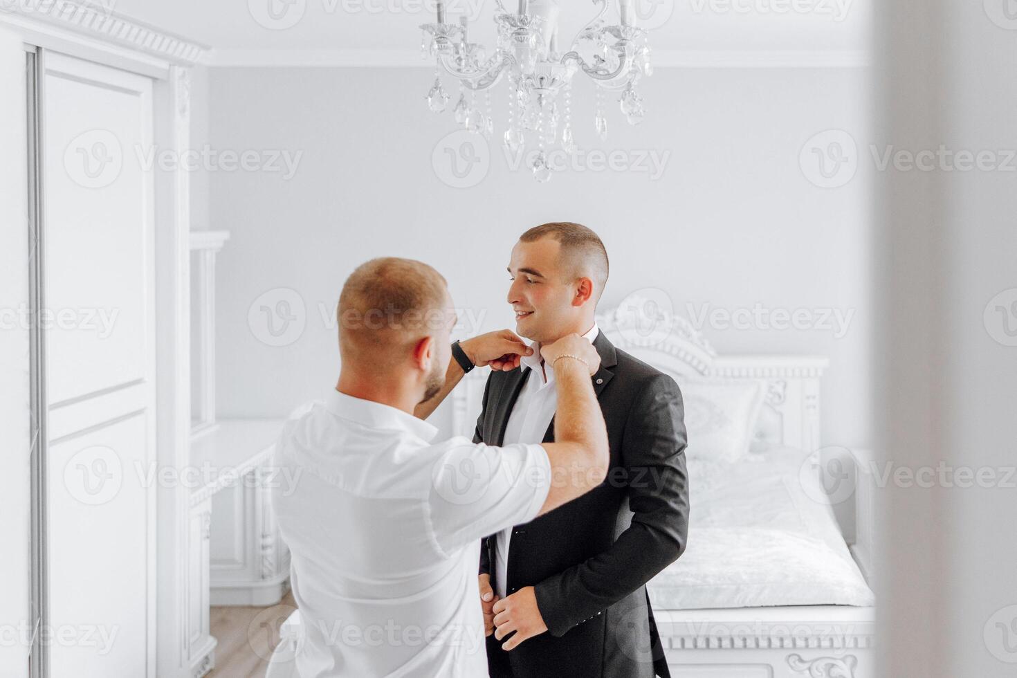 Two men are getting dressed up in a bedroom photo
