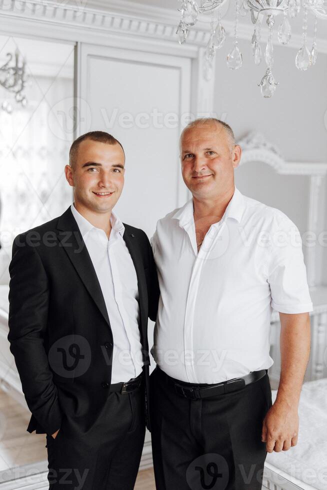 Two men are standing next to each other, one wearing a suit photo