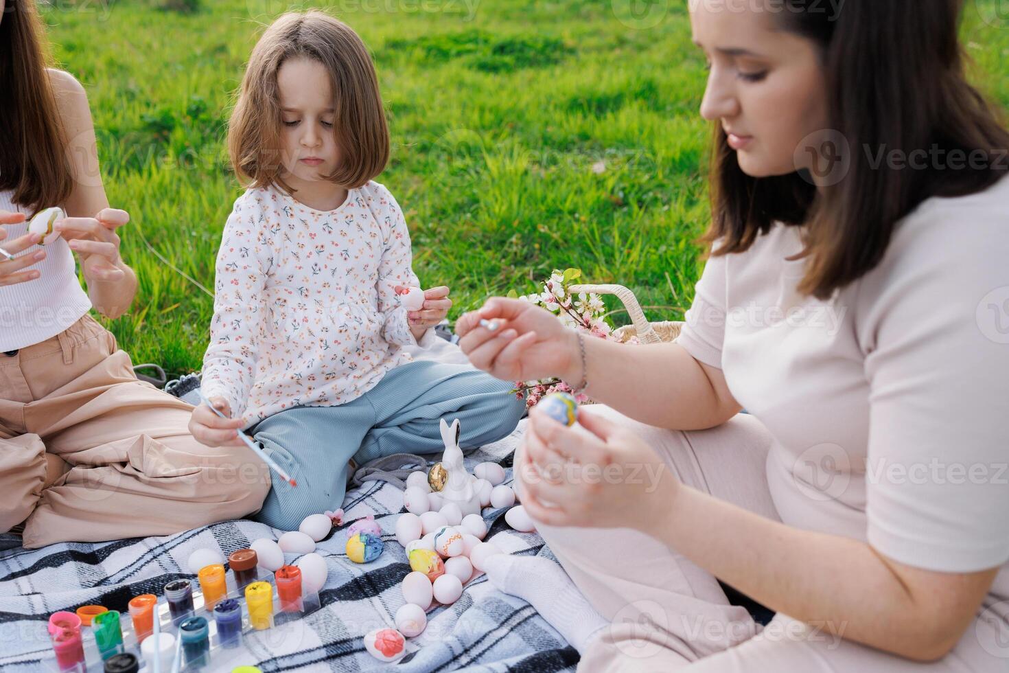 A woman and two children are sitting on a blanket in a grassy field photo