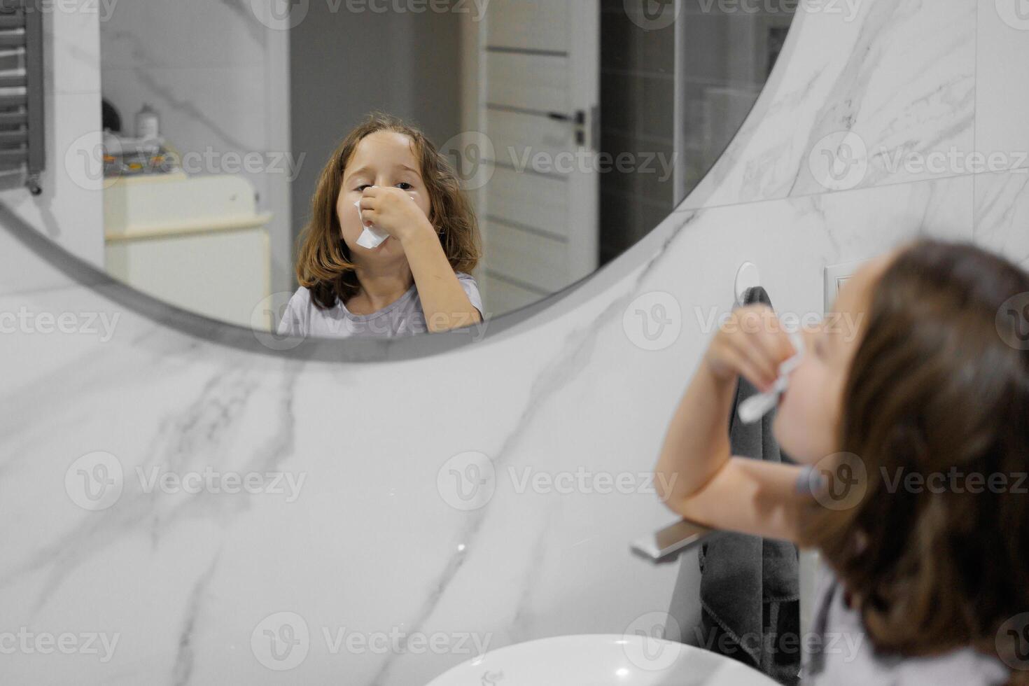 A young girl blows snot from her nose in front of a mirror photo