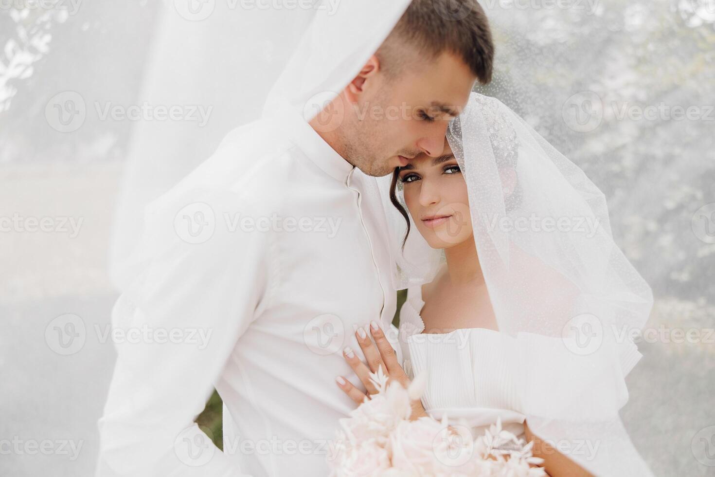 A bride and groom are embracing each other in a white wedding dress and suit photo