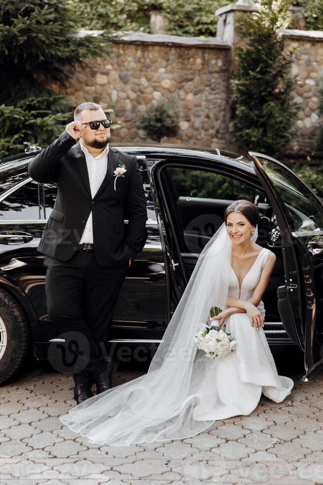 A man and a woman are posing for a picture in front of a black car photo