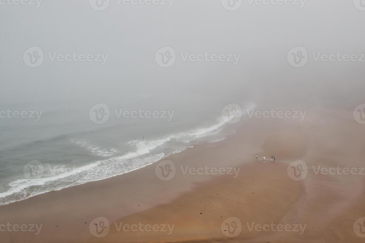 Foggy beach with waves and walkers photo