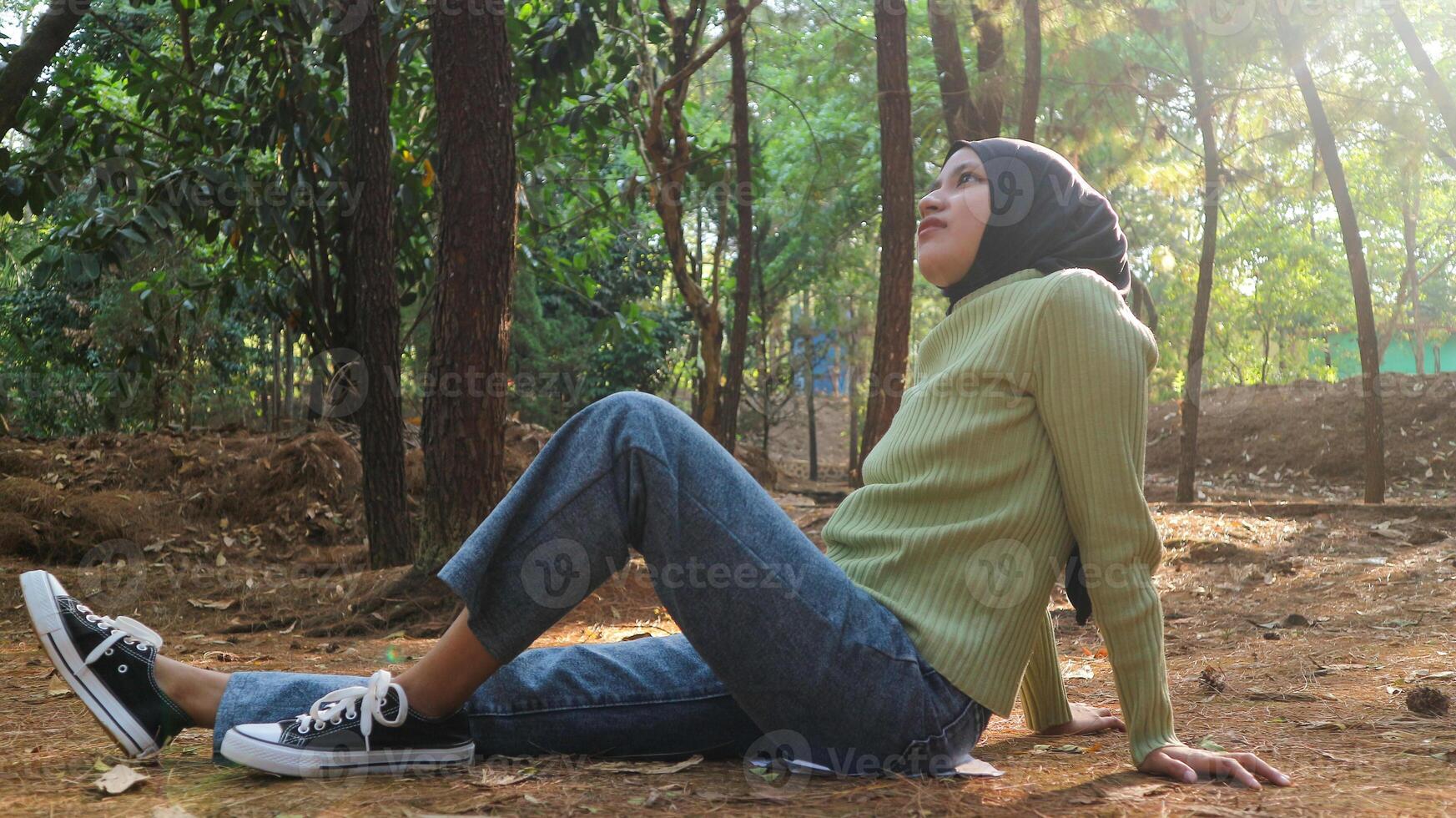 Young muslim woman sitting on grass resting carefree, relaxing on lawn on sunny day. Side view photo