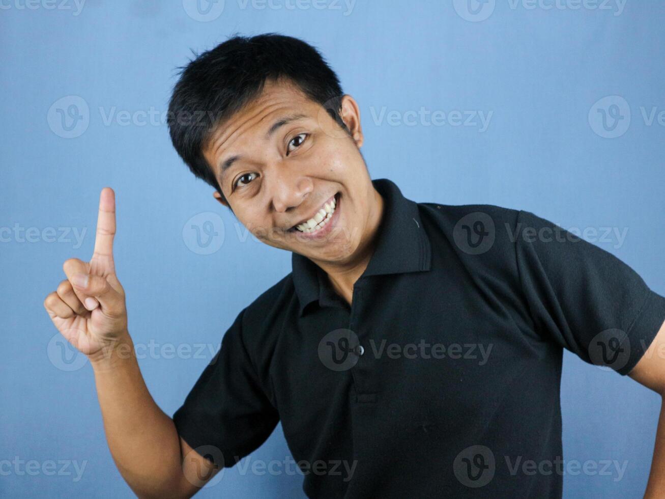 funny face expression of asian man in black shirt smiling, looking at camera while pointing up. photo