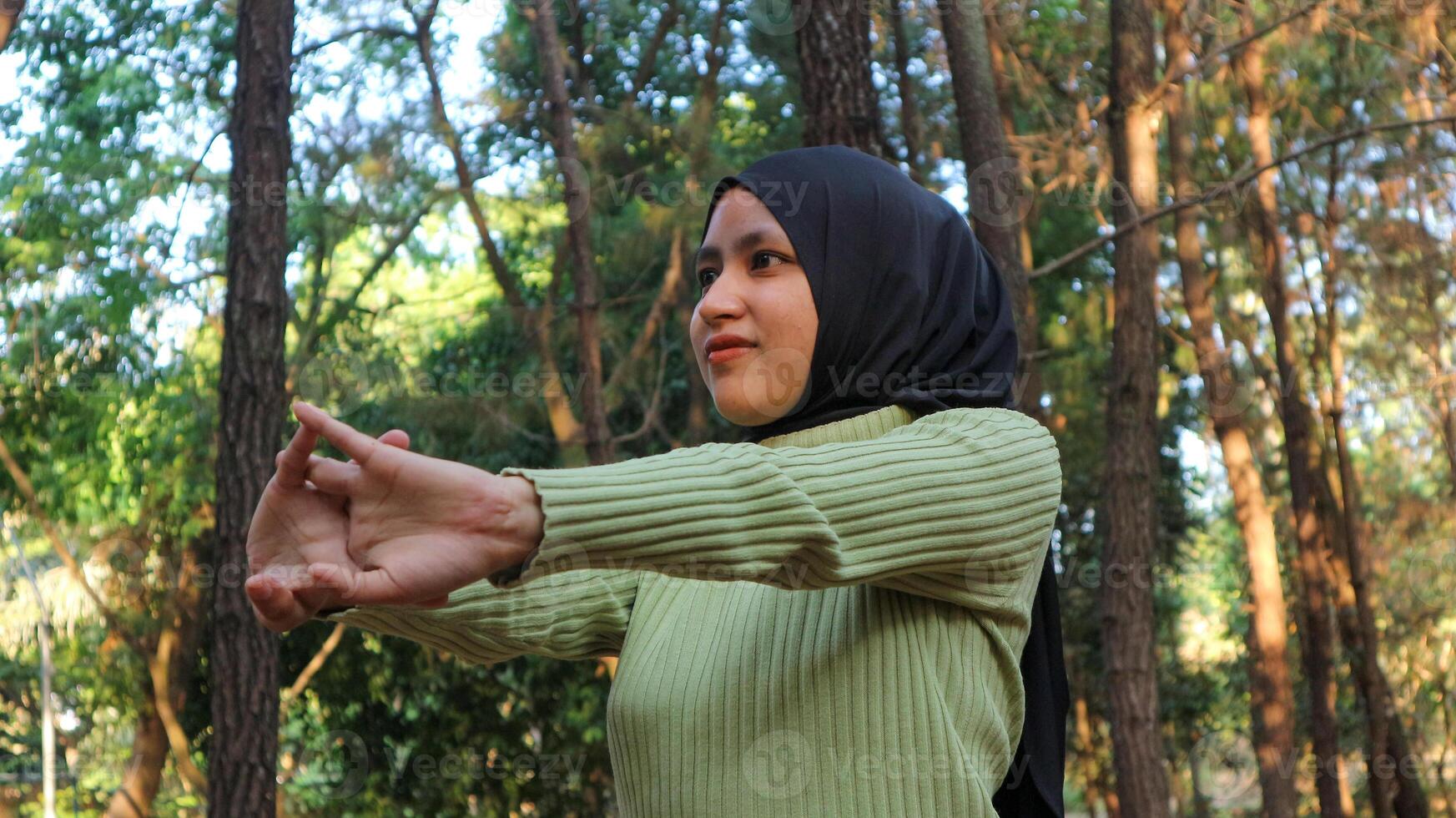 Muslim Women stretching arms and breathing fresh air in middle of pinewood forest while exercising photo