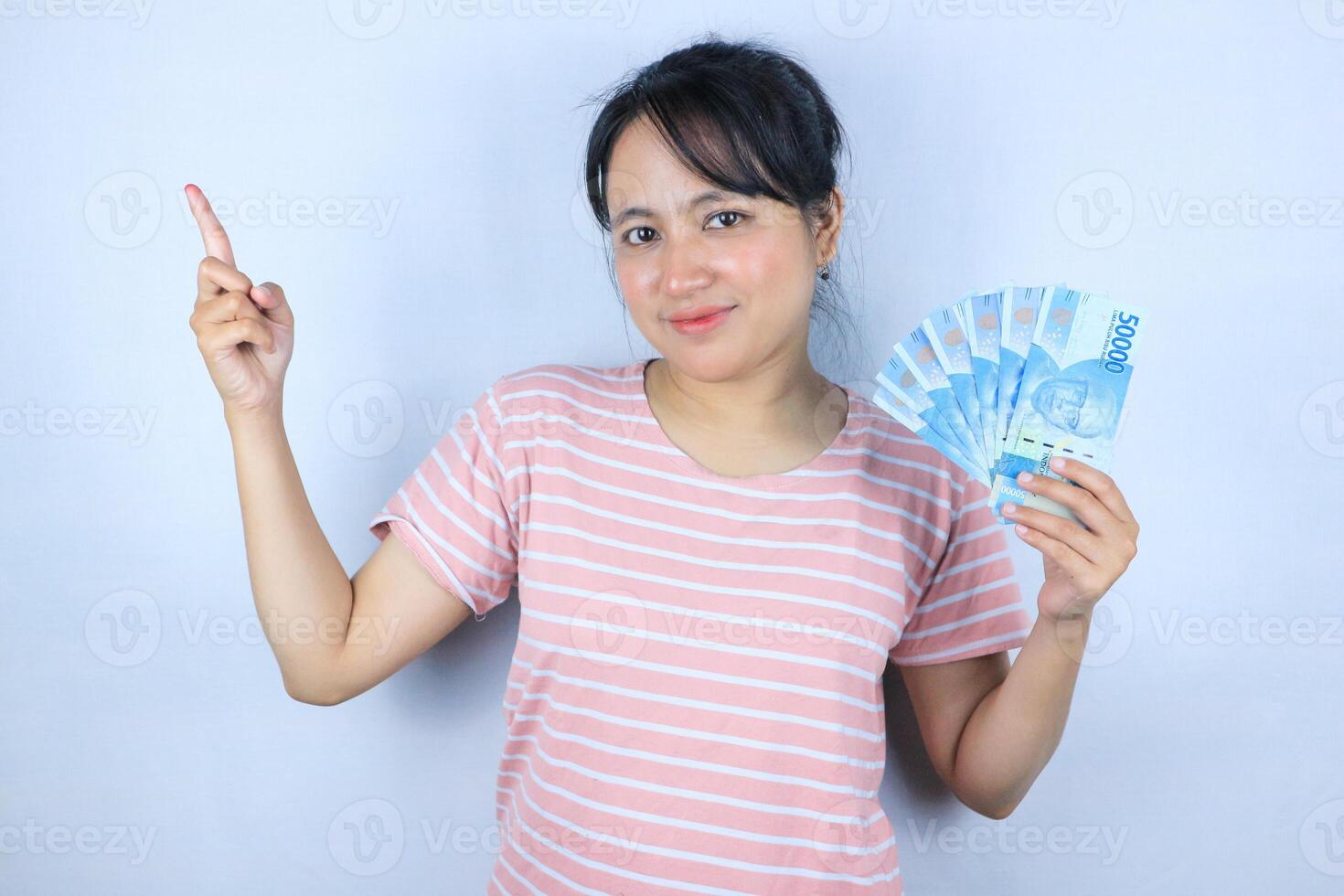 Portrait of a young asian woman holding cash money while pointing empty space. Advertisement concept photo