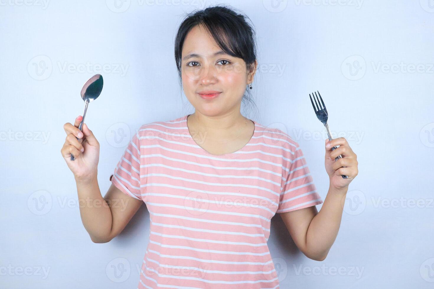 smiling expression of young asian woman looking at the camera while holding a fork and spoon photo