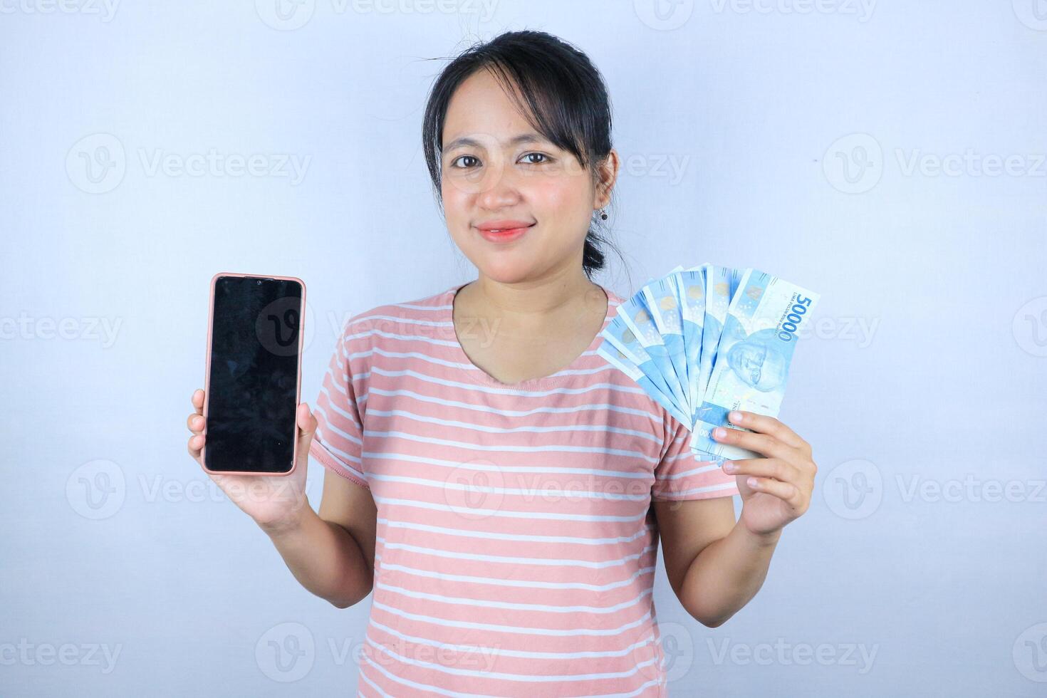 smiling expression of asian woman holding cash rupiah and showing empty mobile screen. photo
