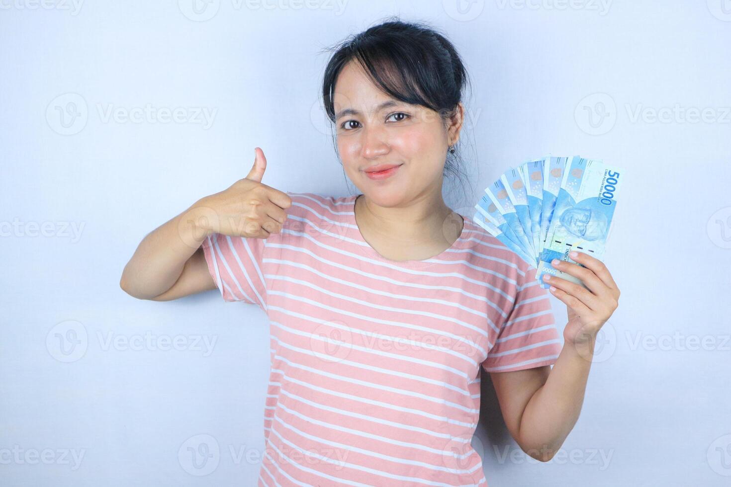 Portrait of a young Asian woman holding cash while giving a thumbs up. Advertising concept photo