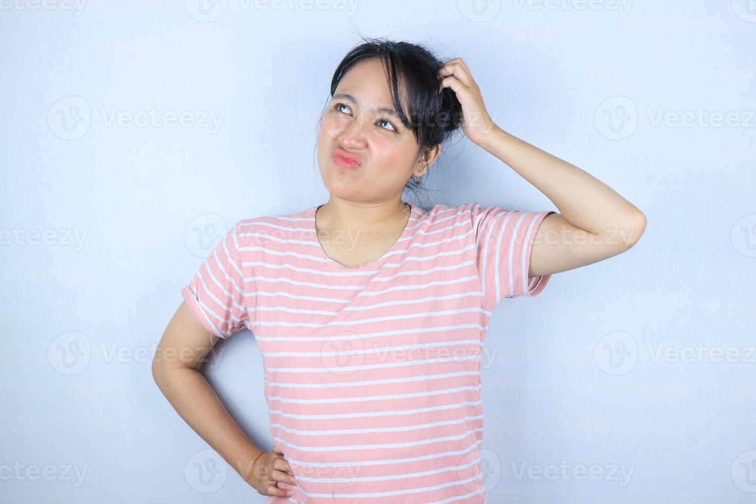 Confused expression of beautiful Asian woman scratching her head while looking up photo