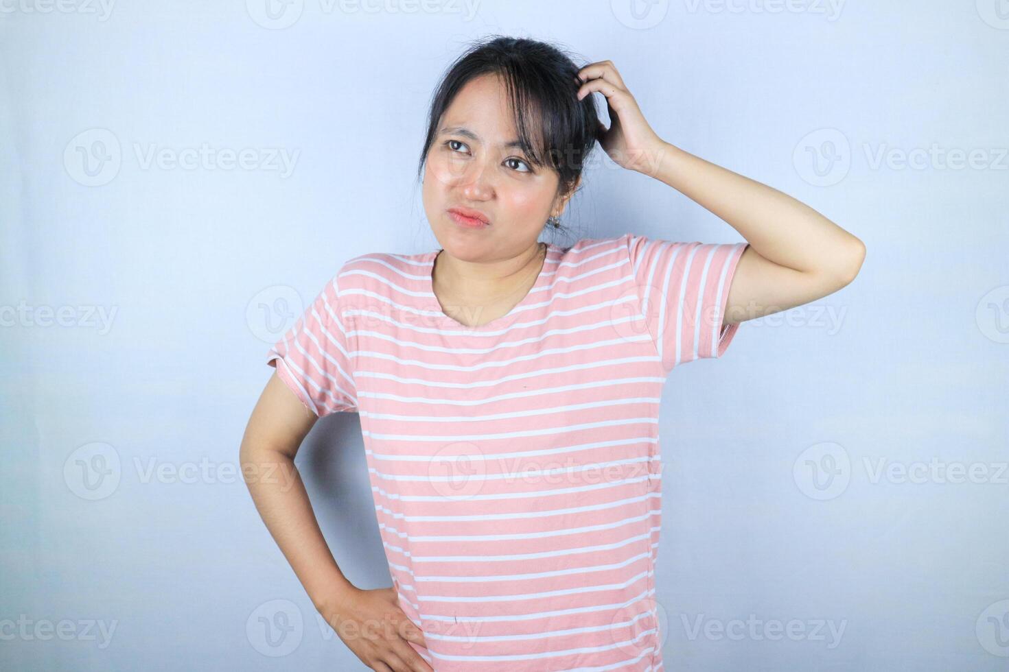 Confused expression of beautiful Asian woman scratching her head while looking up photo