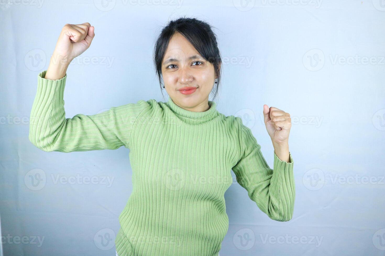 Beautiful Asian woman in a green sweater clenched fists, celebrating victory expressing success photo