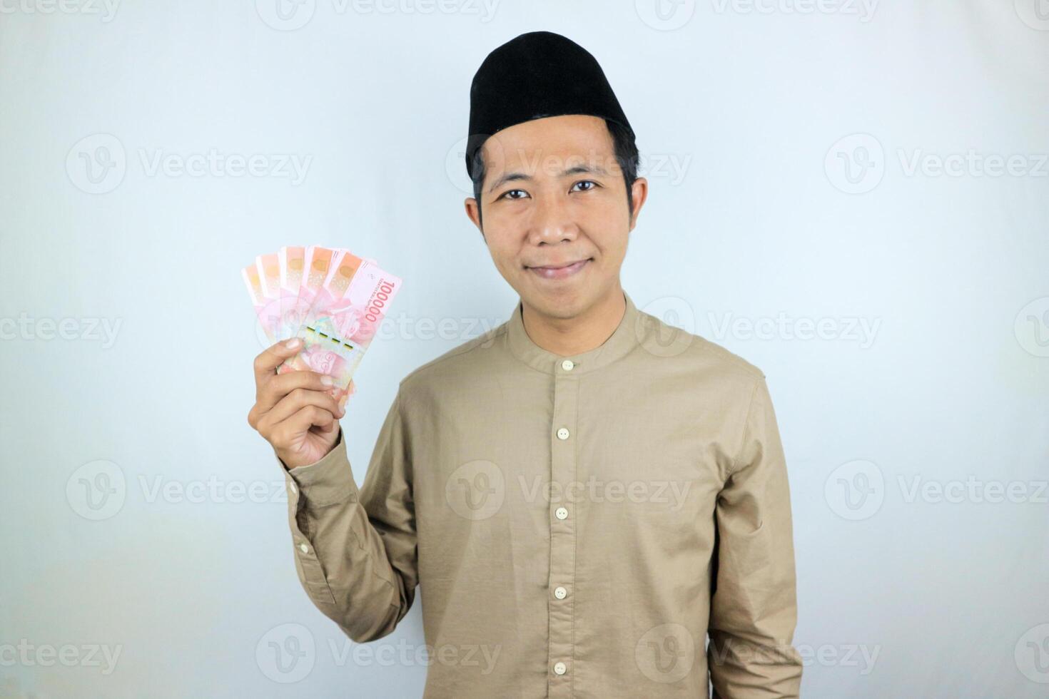 Happy expression of Asian Muslim man holding money rupiah banknotes isolated on white background photo