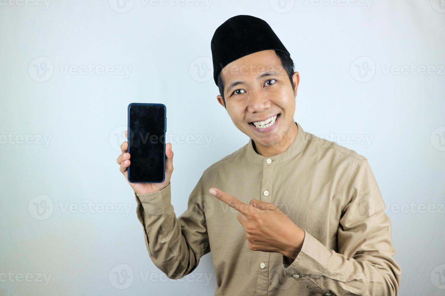 Smiling happy of muslim asian man wearing cap showing empty phone screen. Advertising concept photo