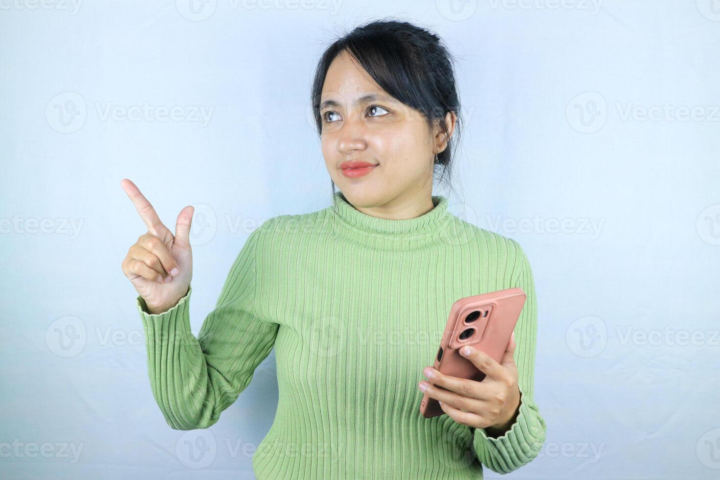Smiling asian woman holding smart phone while pointing finger on white background photo