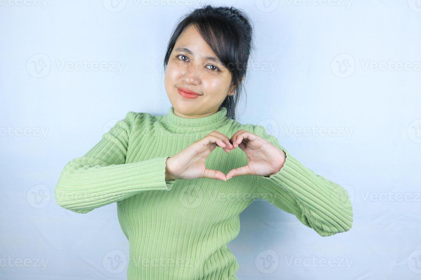 Smiling young asian woman making a heart gesture with her fingers in front of her chest photo