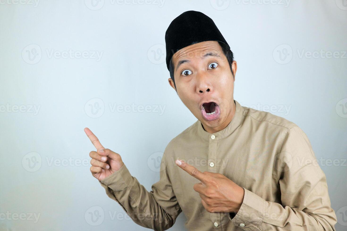 funny facial expression shocked and surprise asian muslim men wearing cap pointing aside photo