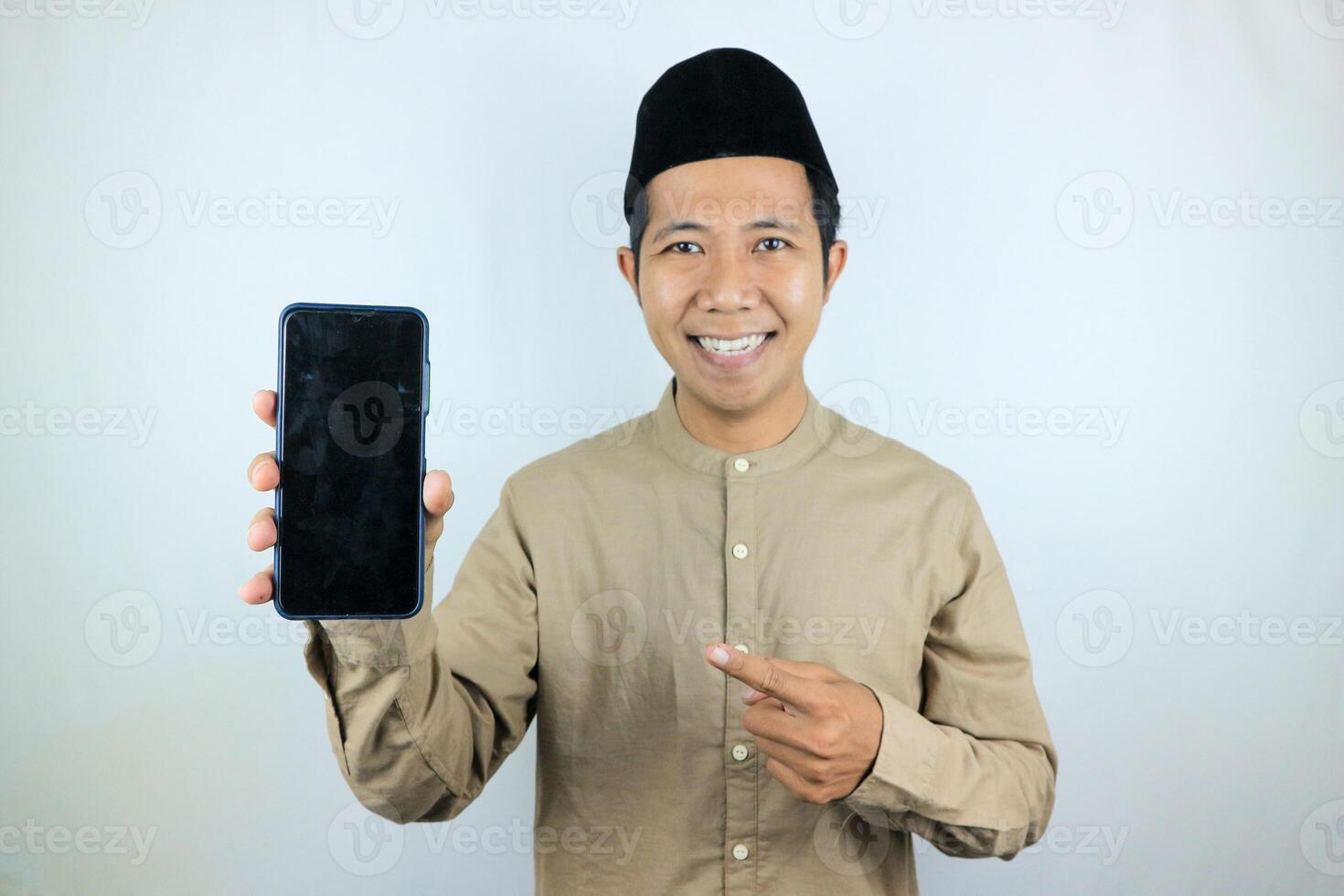 Smiling happy of muslim asian man wearing cap showing empty phone screen. Advertising concept photo