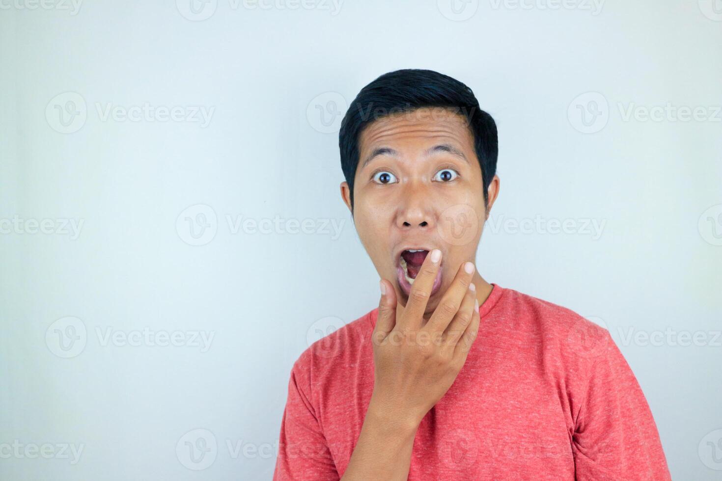 funny expression of shocked and surprised Asian man wearing a red t-shirt looking at the camera photo
