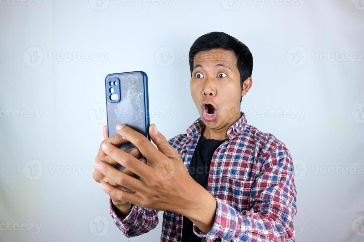 funny facial expression of asian man shocked and shocked holding and looking at phone screen photo