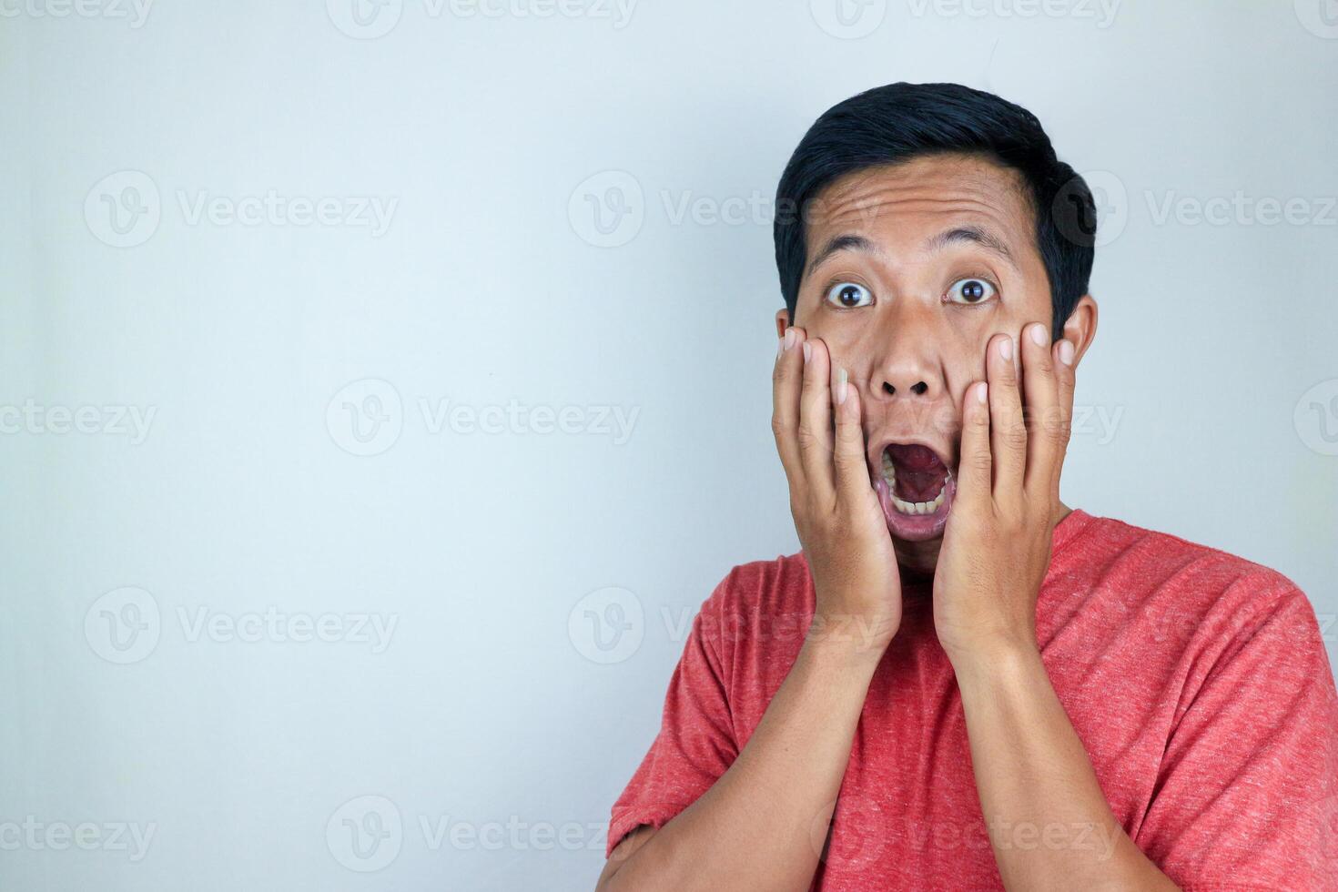 funny expression of shocked and surprised Asian man wearing a red t-shirt looking at the camera photo