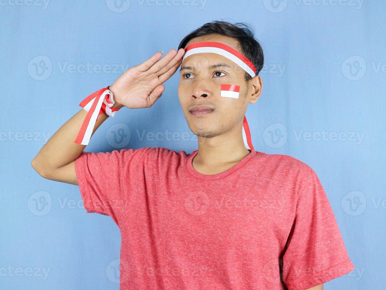 Serious expression indonesian man wearing red and white headband posing to salute indonesian flag photo