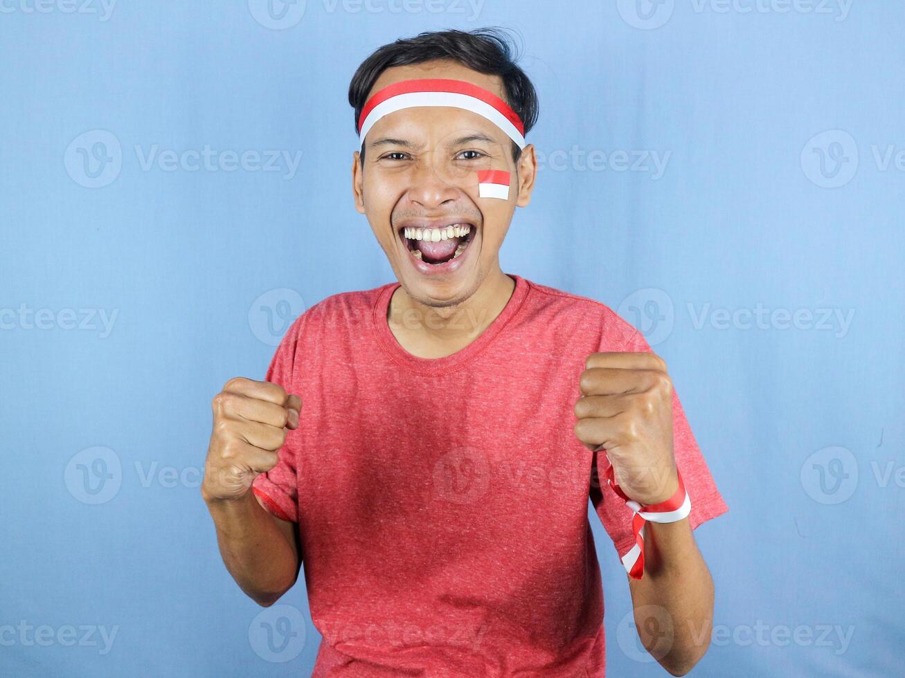 Excited expression young indonesian man wearing red and white headband with clenching fist gesture. photo